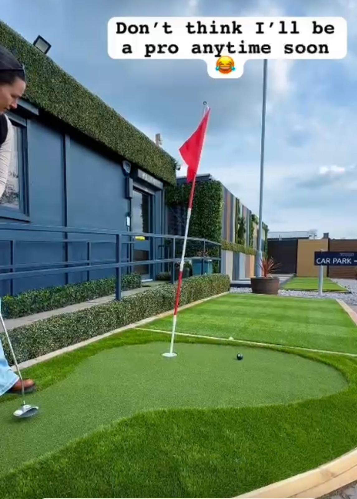 Person playing mini golf with text overlay 'Don't think I'll be a pro anytime soon' on a green putting green.