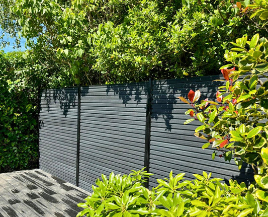 An anthracite composite slatted fence with black metal posts pictured on a sunny summers day with by a customers decked area.