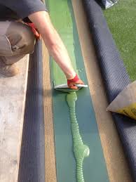 A man spreads out artificial grass adhesive along the fake grass joint tape ready for joining the two pieces of artificial grass.