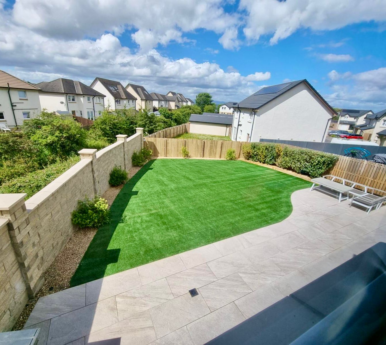Coll 40mm artificial grass pictured in a customers back garden in Glasgow on a summers day with seating area and porcelain paved patio area.