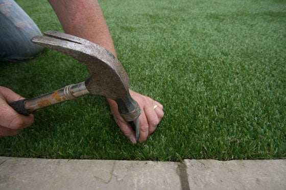 A man nails in an artificial grass pin to secure the fake synthetic grass in place.