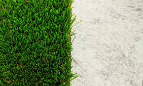 A piece of artificial grass sits on top of a piece of white non woven artificial fake grass membrane.