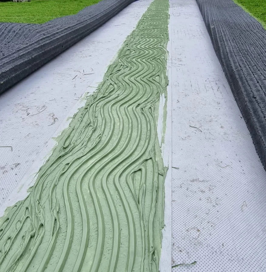 A join of artificial grass being worked on, grass joint tape has been rolled out and artificial grass adhesive spread out ready for the fake grass ready to be joined.