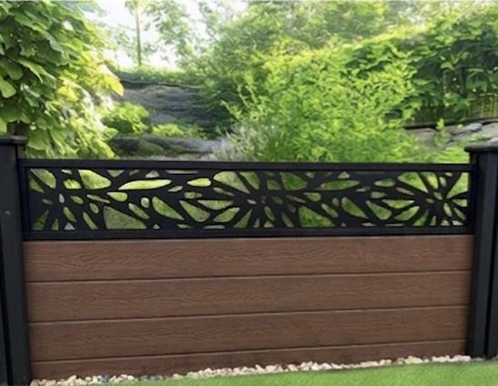 Composite fence with decorative metal top in a garden setting.