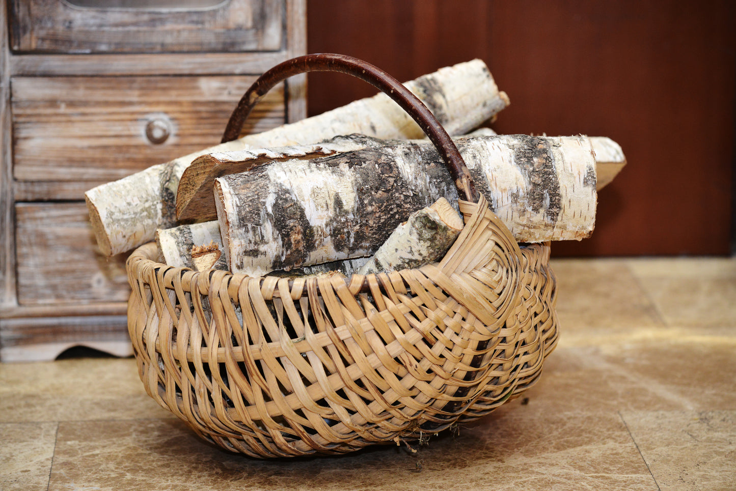 A log basket filled with birch firewood sits in front of a small cabinet,