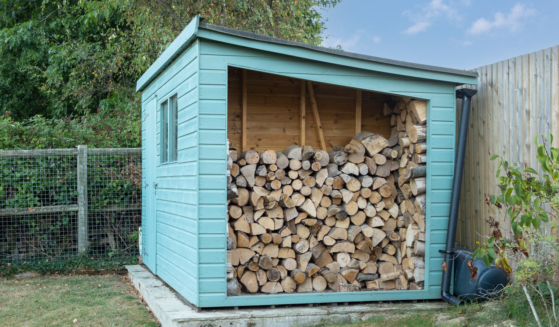 A large shed painted light blue and converted to a firewood log store.