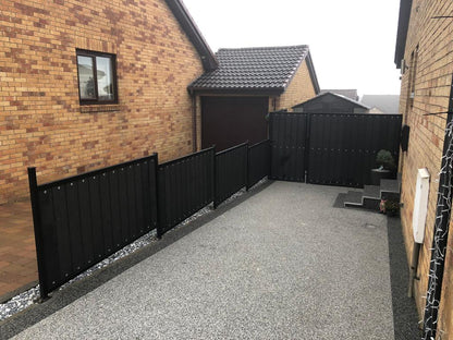 A black or charcoal composite fence on a slop going from 4ft high to 6ft at the back with a matching black composite gate.