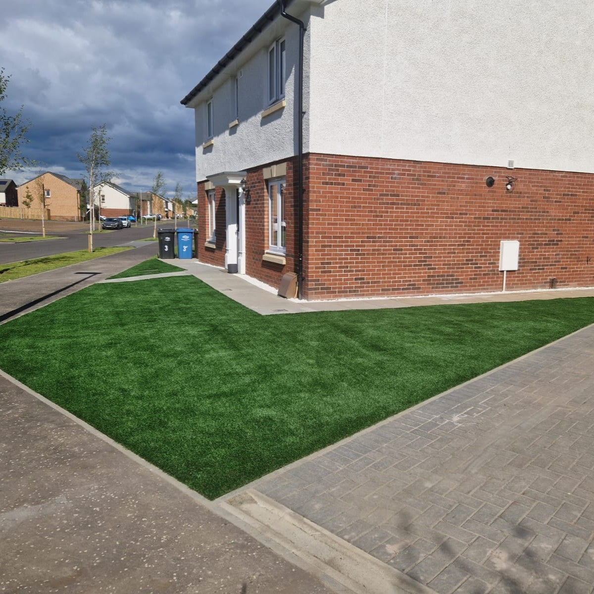 Artificial grass installed in front of a house with a brick and concrete exterior.