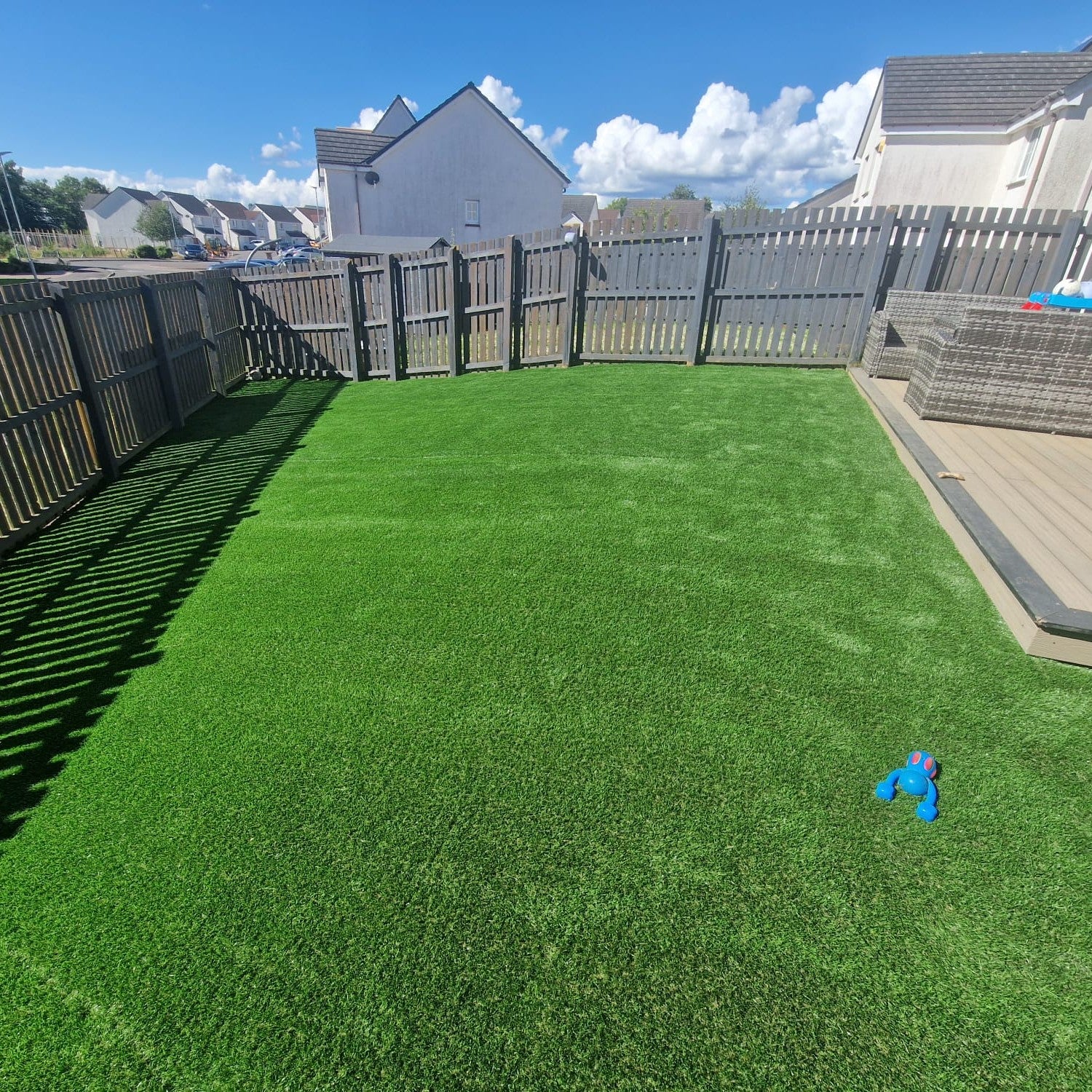 Backyard with artificial grass, wooden fence, and blue toy on a sunny day.