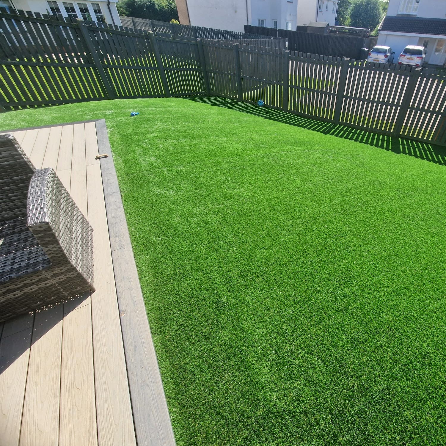 Green artificial lawn with a composite deck in a residential backyard.