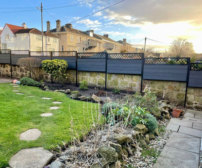 A large anthracite staggered fence raised to sit on top of a sandstone wall with traditional black fence topper.