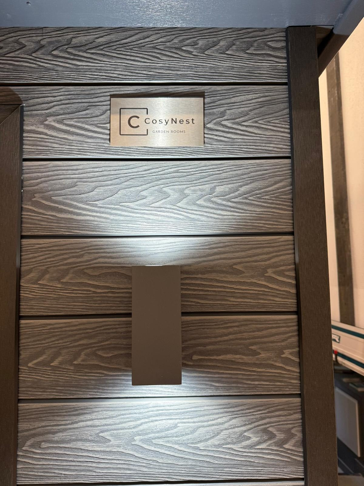 Composite Clad garden room with 'CosyNest' branded plaque and up lighter.