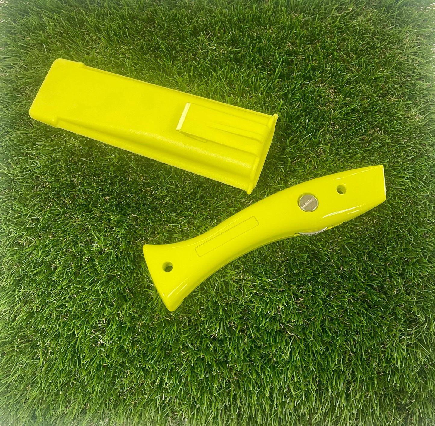 A yellow artificial fake grass cutting knife with holster laying on fake grass.