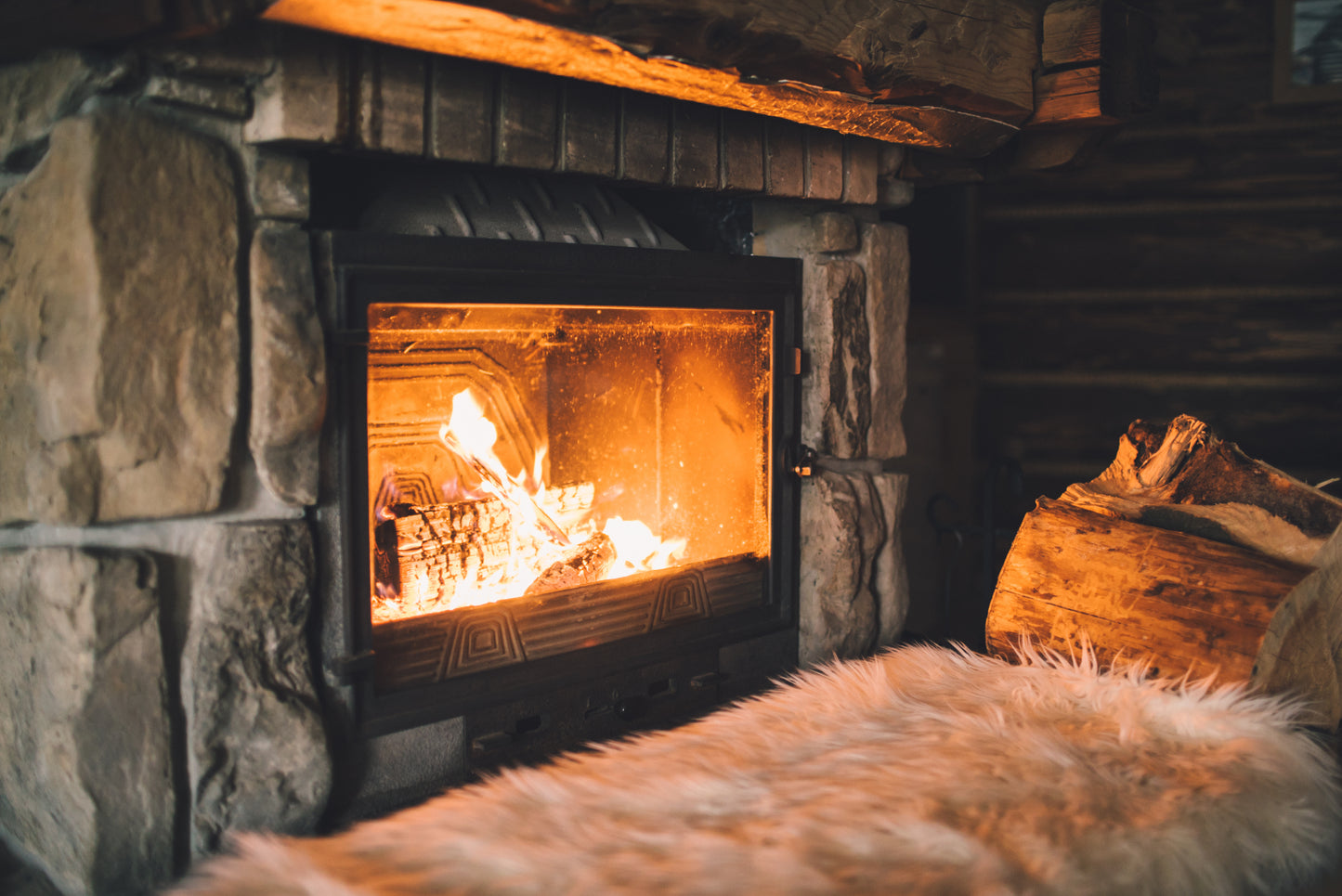 A large wood burning stove alight and burning away with a few logs stacked to the side.