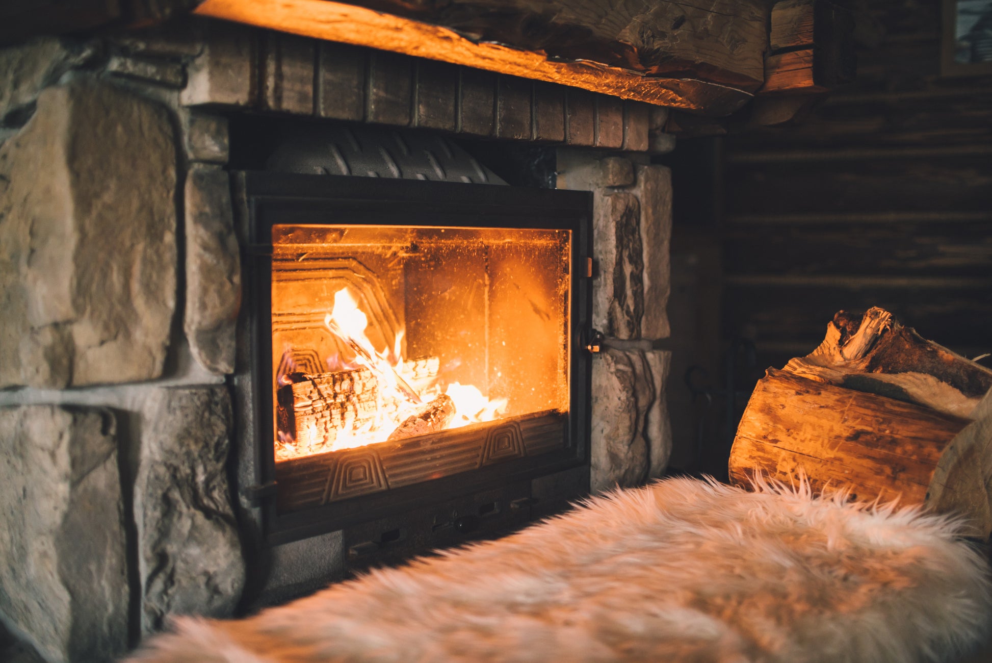 A large wood burning stove alight and burning away with a few logs stacked to the side.