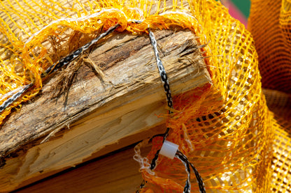 An open orange net of oak firewood.