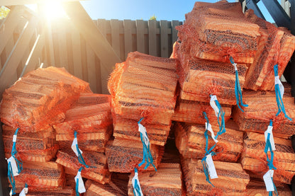 A pallet of of orange firewood log nets stacked up with the sun bursting through from behind.