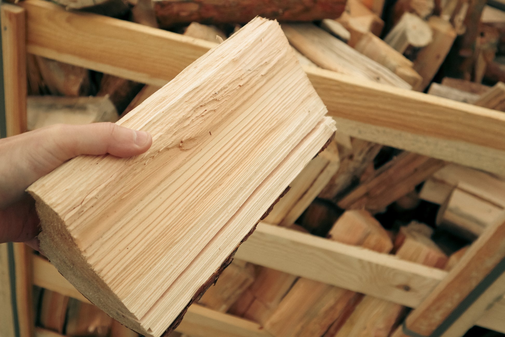 A man holds a split firewood log showing the wood grain.