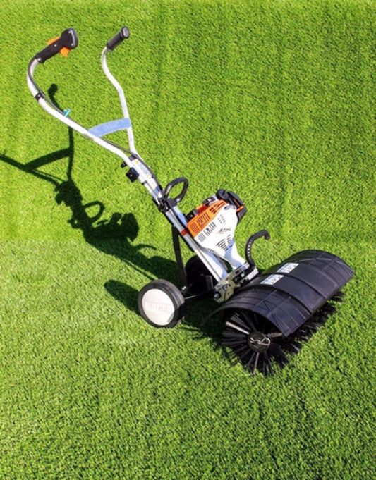 AN artificial grass power brush sitting on fake grass in the sun.